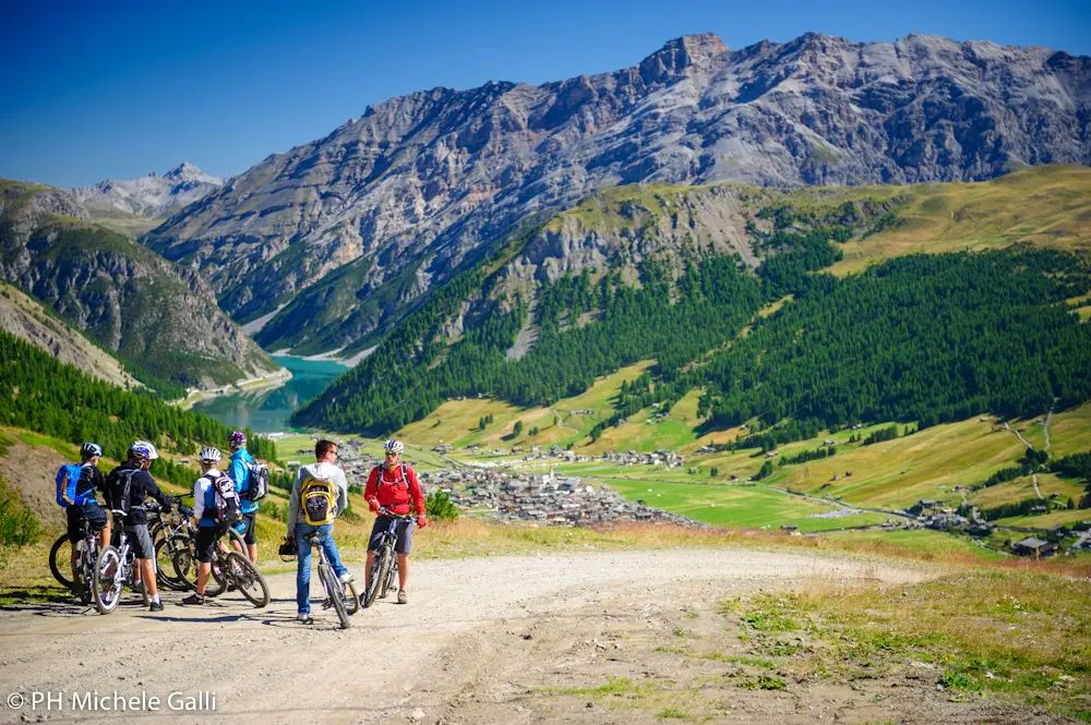 Ciclisti in pausa con vista panoramica sulle montagne e una valle verde.