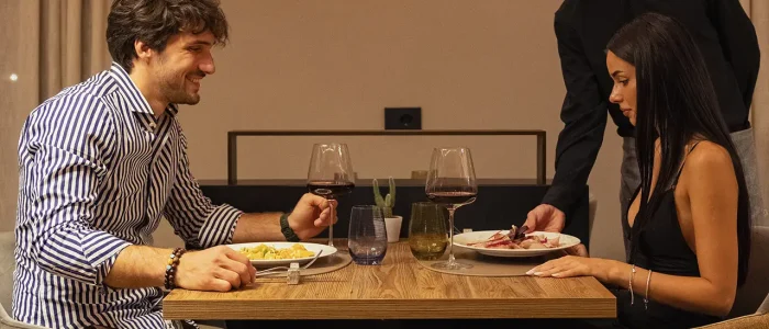Due persone sedute al tavolo di un ristorante con un cameriere che serve i piatti.