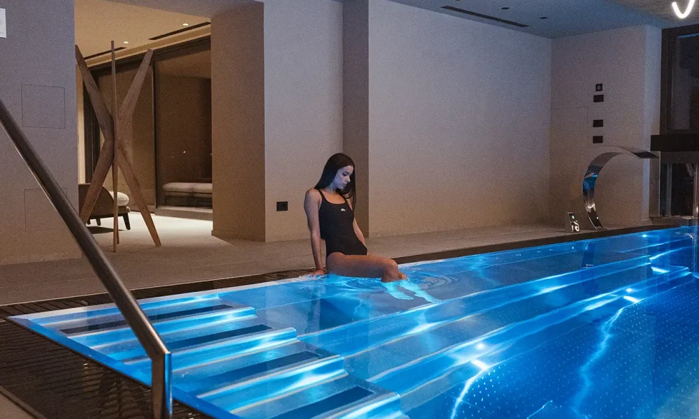 Donna seduta sul bordo di una piscina illuminata in un ambiente moderno.