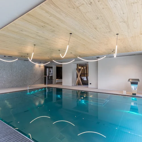 Piscina coperta moderna con illuminazione contemporanea e dettagli in legno.