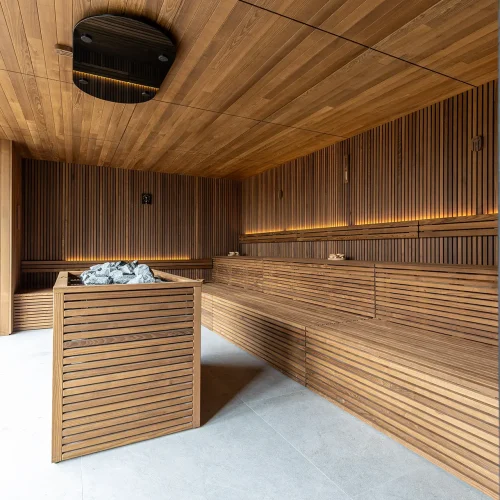 Una sauna moderna con rivestimenti in legno e pietre laviche al centro.