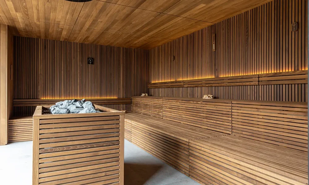 Una sauna moderna con rivestimenti in legno e pietre laviche al centro.