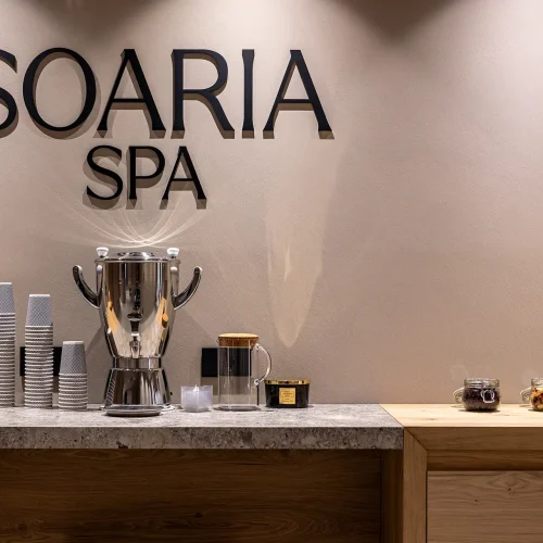 Postazione per bevande alla "Soaria Spa" con termos, bicchieri e barattoli di snack su un bancone.