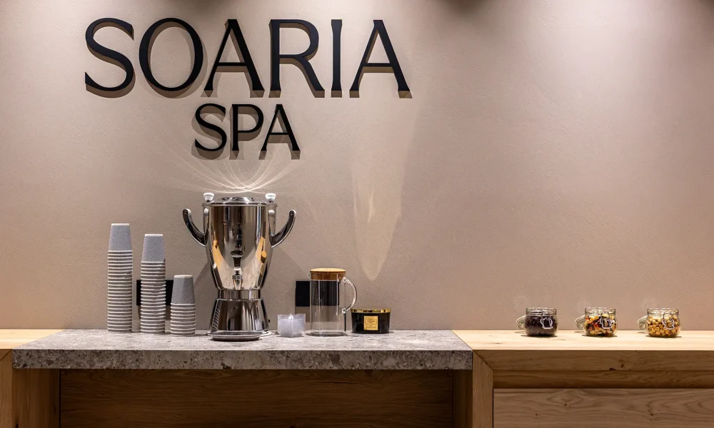Postazione per bevande alla "Soaria Spa" con termos, bicchieri e barattoli di snack su un bancone.