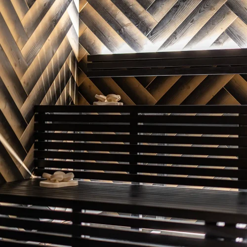 Interno di una sauna moderna con panchine in legno scuro e pareti a motivo chevron.