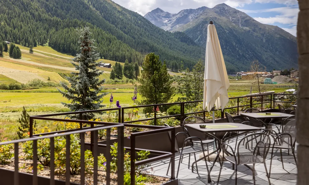 Terrazza con tavoli e sedie affacciata su un paesaggio montano verde.