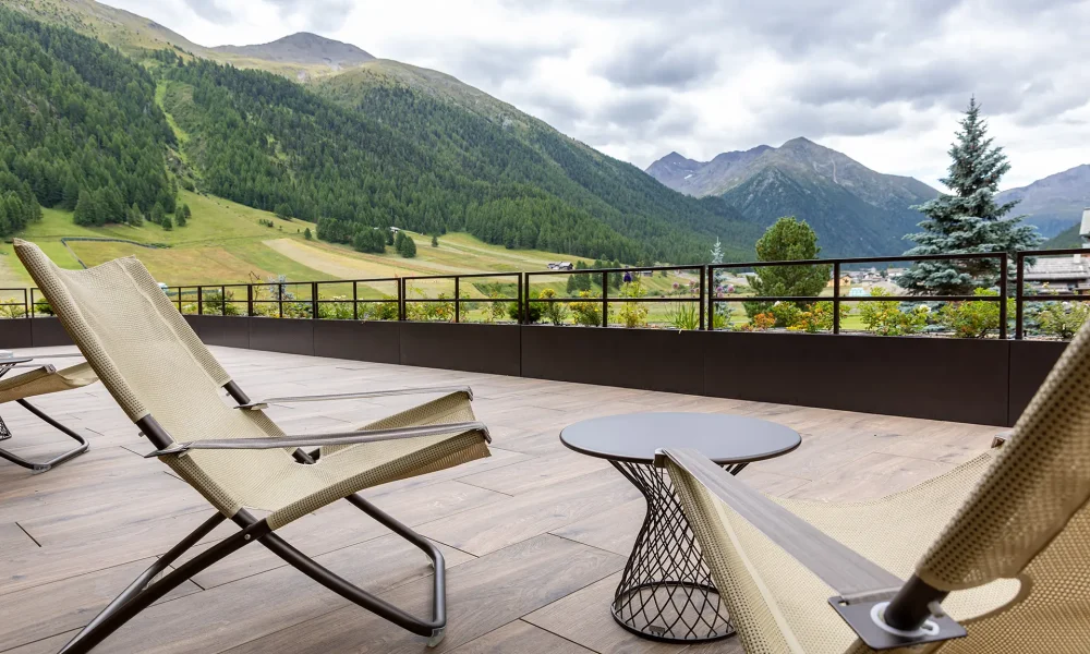 Terrazza moderna con lettini e vista panoramica sulle montagne verdi.