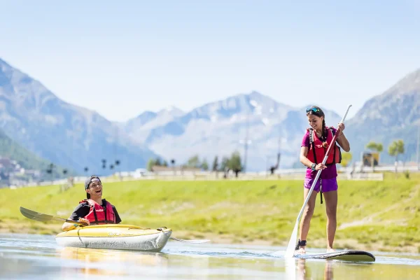 Due persone si godono attività acquatiche su un lago di montagna, una in kayak e l'altra su un paddleboard.