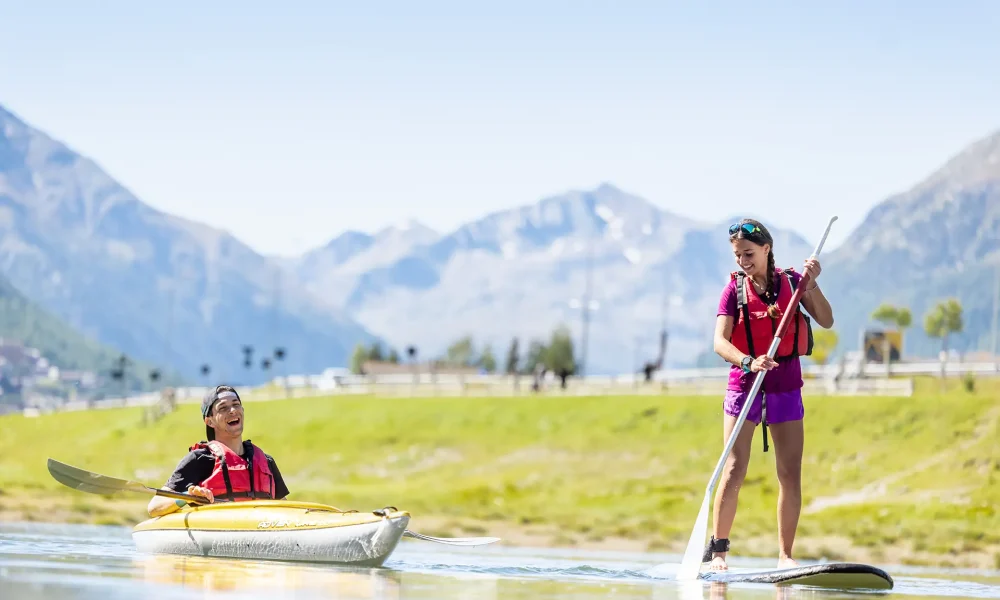 Due persone si godono attività acquatiche su un lago di montagna, una in kayak e l'altra su un paddleboard.