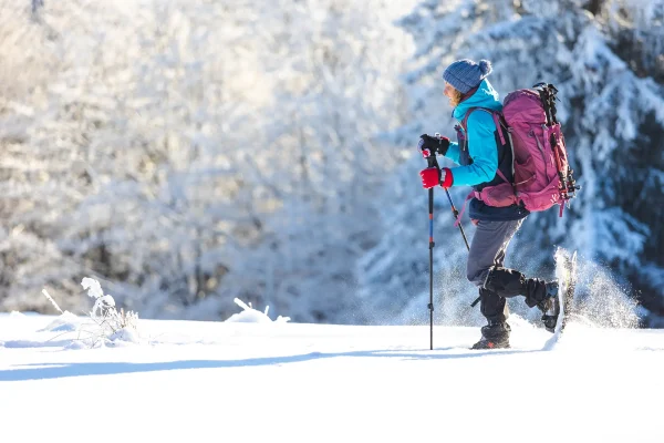 Persona che cammina con le ciaspole sulla neve in una foresta invernale.